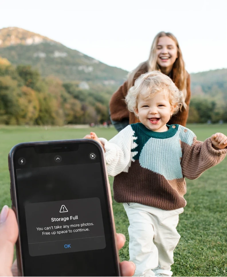 A phone showing 'Storage Full' as a laughing toddler runs toward it across a field