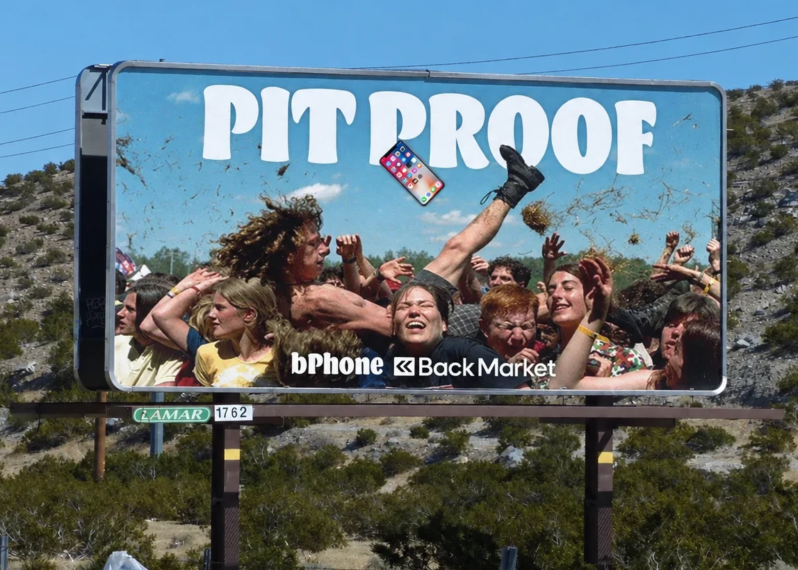 Desert highway billboard: a festival crowd mid-mosh with a phone flying through the air, 'PIT PROOF', bPhone by Back Market