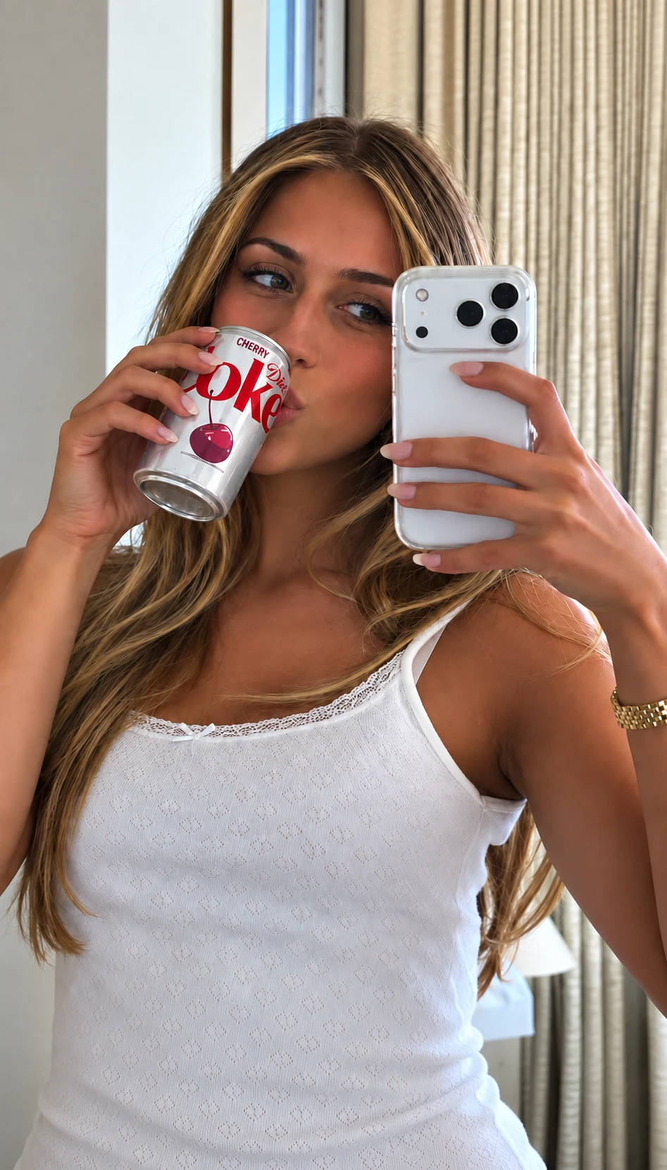 A mirror selfie of a woman sipping from a can of Diet Coke Cherry