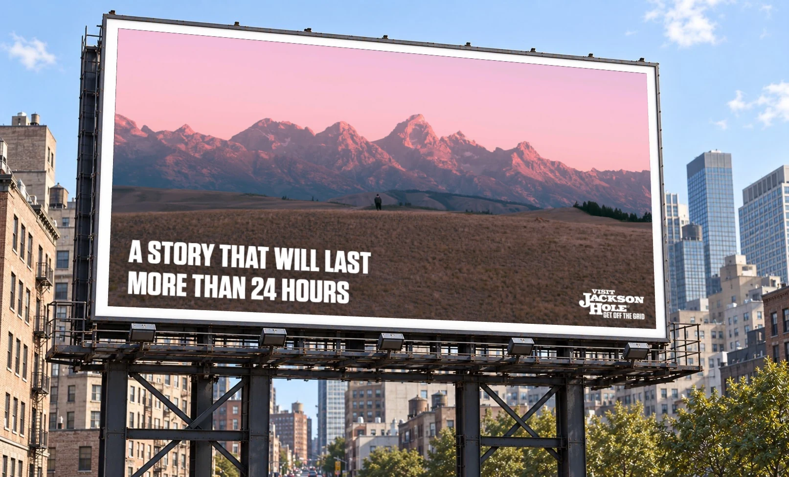 Billboard: 'A story that will last more than 24 hours,' over the Tetons at pink dusk with a lone figure in a field