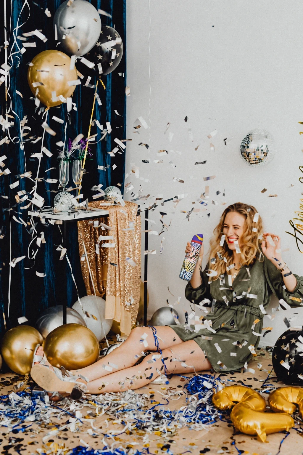 The same woman laughs on the floor in a shower of confetti, holding her Owala among balloons and streamers