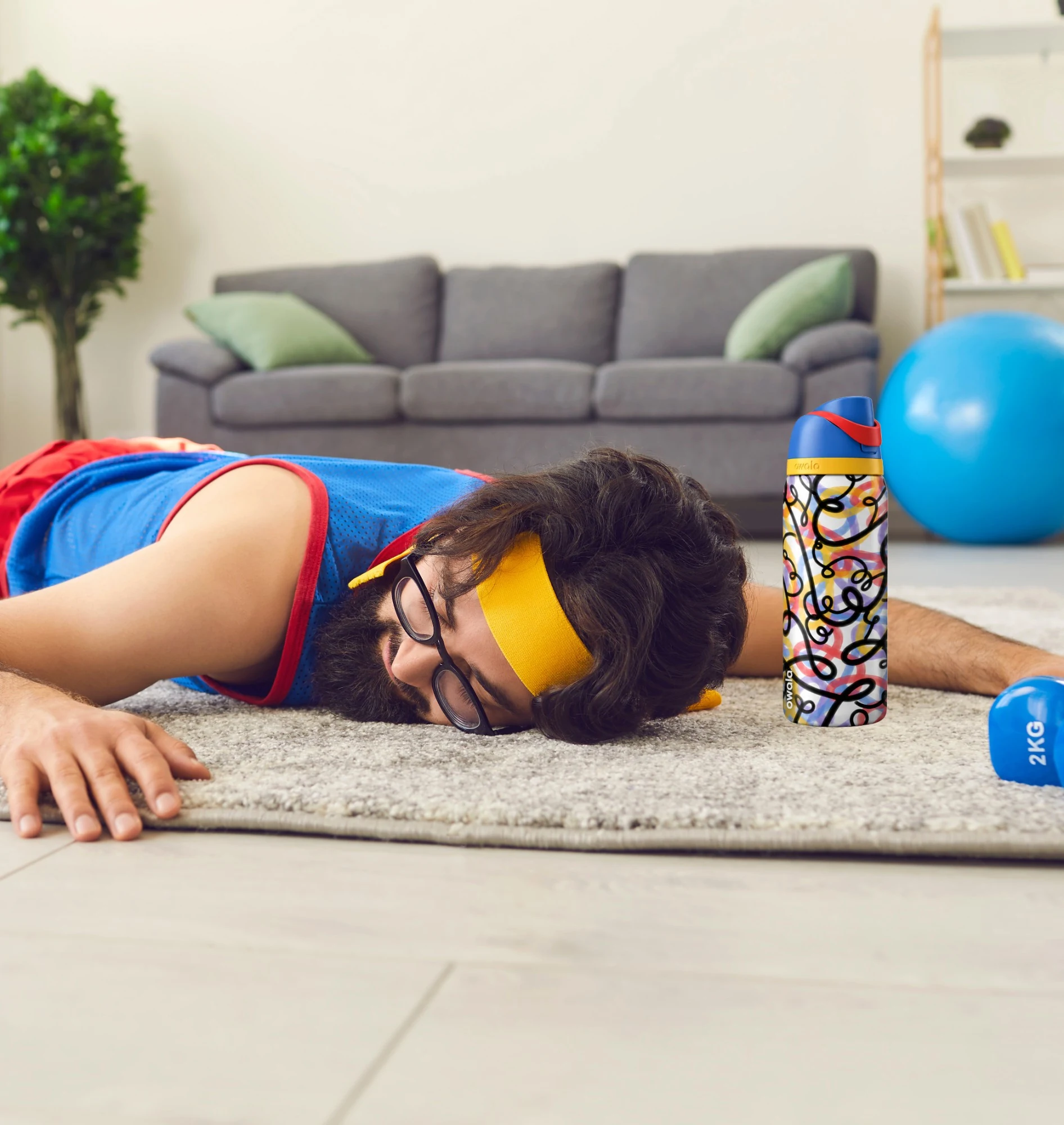 Hardly working: the same man lies face-down on the rug in a headband, his Owala standing beside him